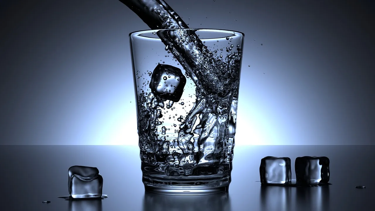 glass of ice water with ice cubes on wooden table